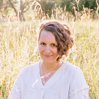 Corinna Fanni, Coach für Nervensystemregulation und emotionale Balance sitzt in der Abendsonne in einer Sonnen beschienen Wiese.