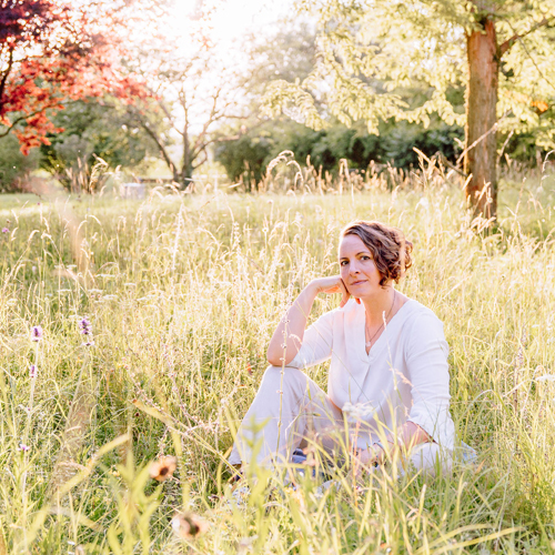 Corinna Fanni, Coach für Nervensystemregulation und emotionale Balance sitzt in der Abendsonne in einer Sonnen beschienen Wiese.