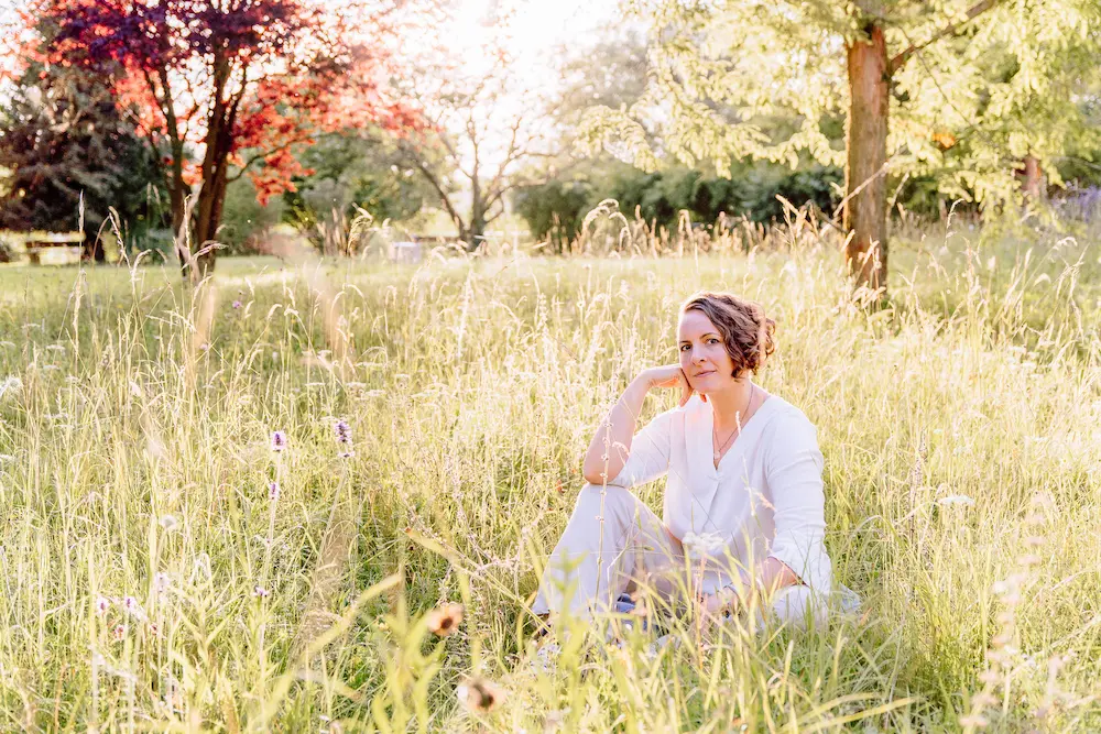 Corinna Fanni, Coach für Nervensystemregulation und emotionale Balance sitzt in der Abendsonne in einer Sonnen beschienen Wiese.